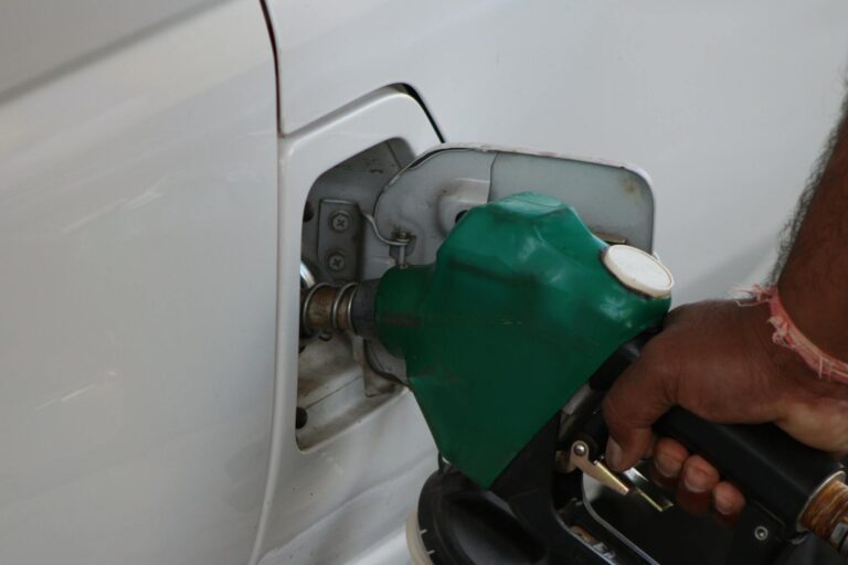 Close-up of a hand refilling a car's gas tank at a station with a green fuel nozzle.
