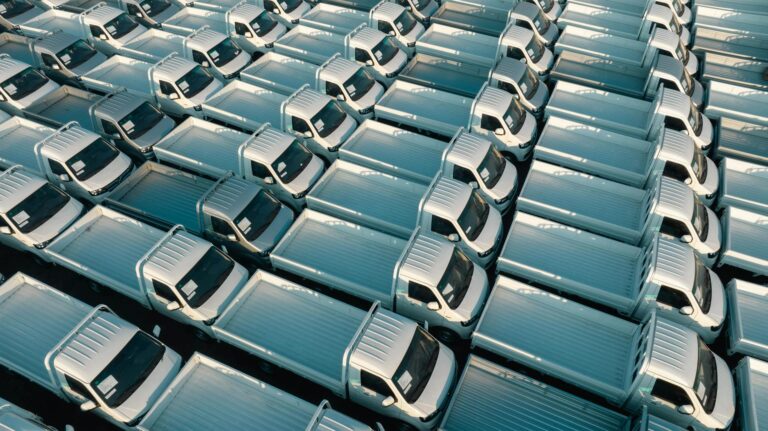 A top-down view of numerous white trucks parked in a grid pattern, showing symmetry and industrial logistics.