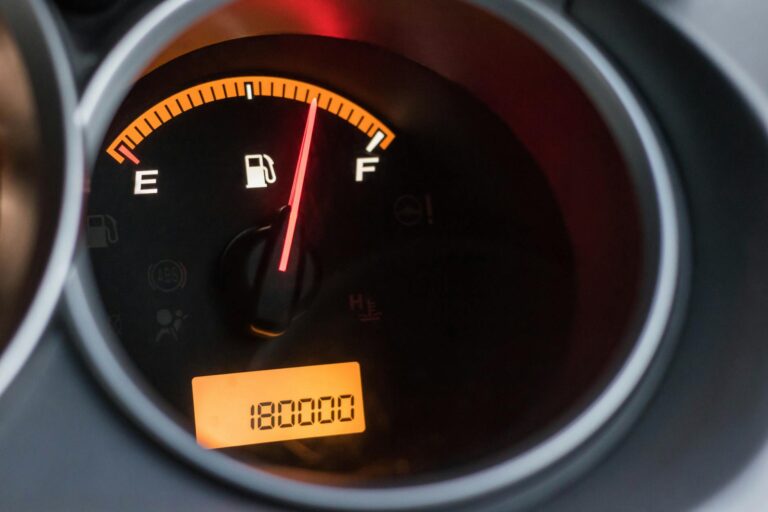 Close-up image of a car's fuel gauge showing a full tank with an odometer reading of 180000 miles.