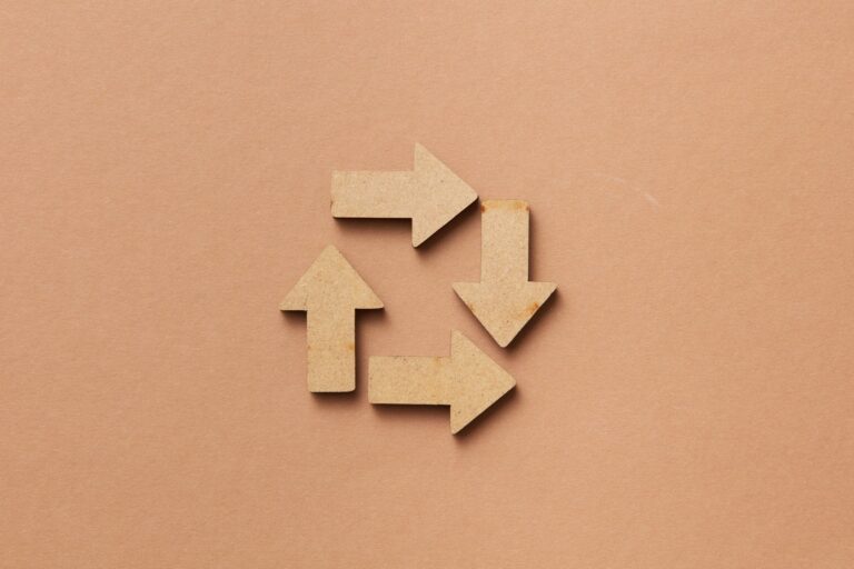Close-up of a recycling symbol made from wooden arrows on a beige background.