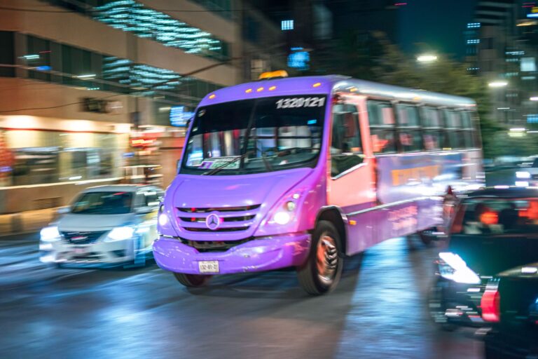 Vibrant bus navigating bustling Ciudad de México street at night, showcasing urban traffic flow.