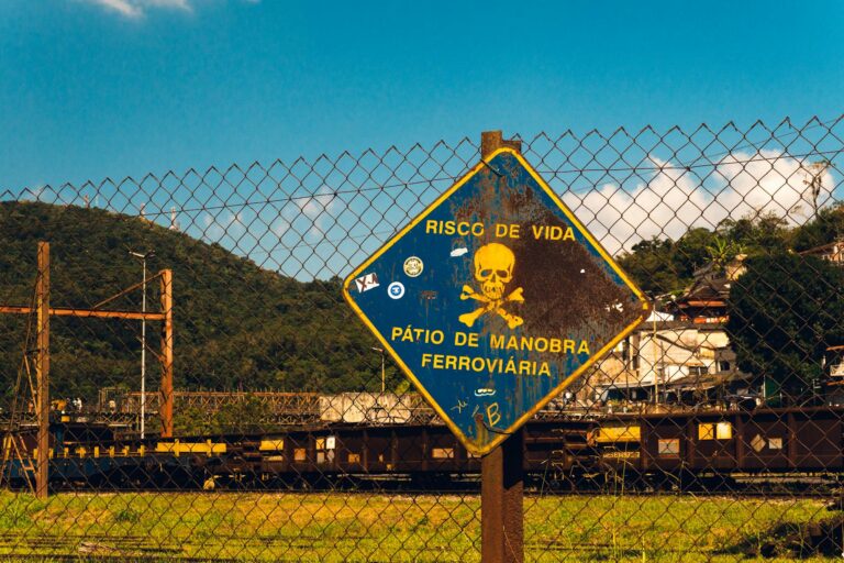 Rusty danger sign at a railway yard in São Paulo, Brazil under a bright blue sky.