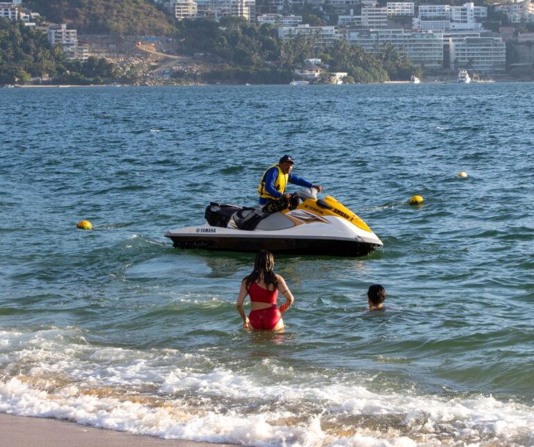 Two people enjoy the water near a jet ski in Acapulco, Mexico, on a sunny day.