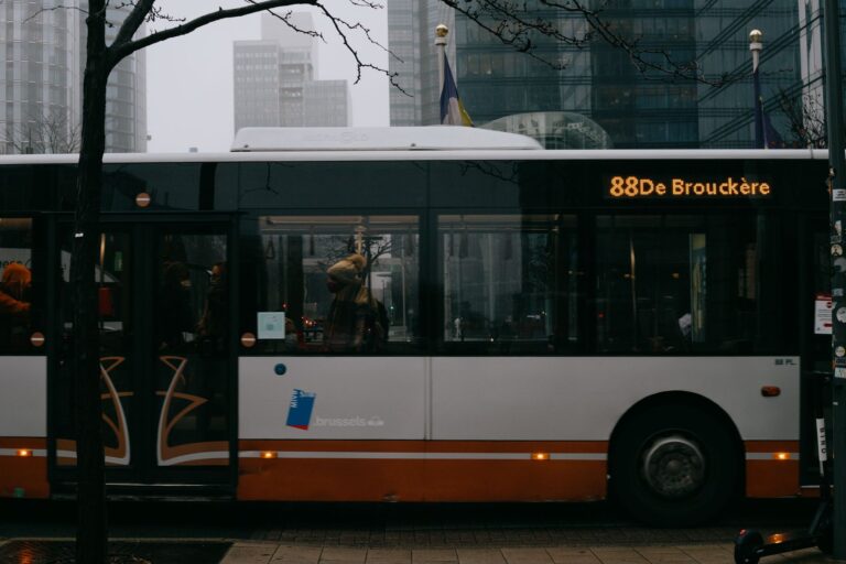 Modern bus with number and inscription on roadway against multistory building facades in city