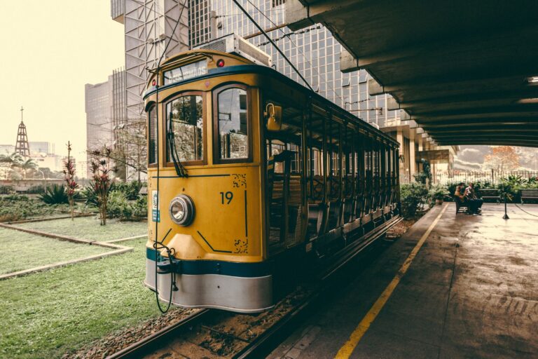 Vintage yellow tram at station in Rio de Janeiro, Brasil, with city architecture in background.