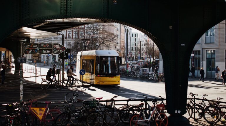 Dynamic street scene in Berlin featuring a yellow tram, bicycles under a bridge, and pedestrians in the city.