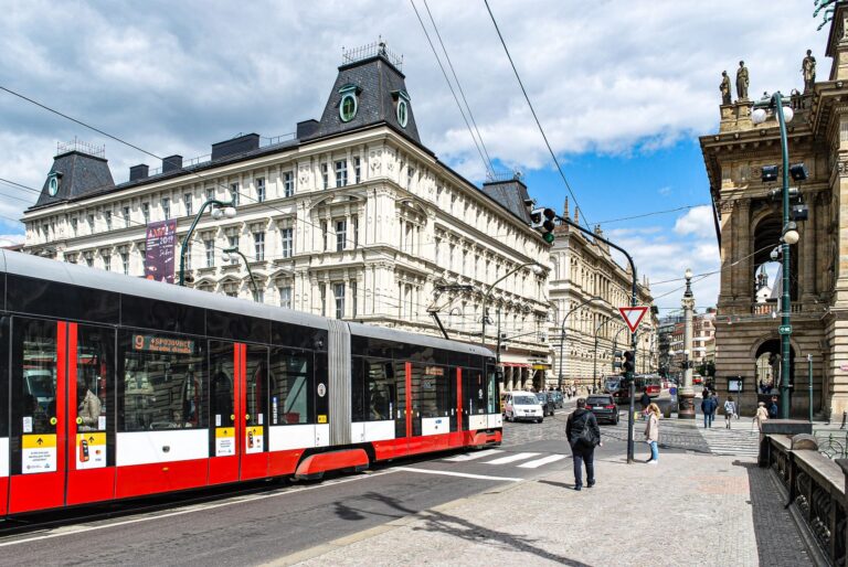Modern tram passing by historic architecture in Prague, showcasing urban transport and elegant buildings.