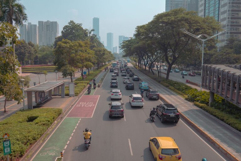 A bustling urban roadway in Jakarta with cars, motorbikes, and a bus stop in view.