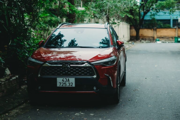 A red Toyota Corolla Cross parked outdoors on a quiet street with greenery.
