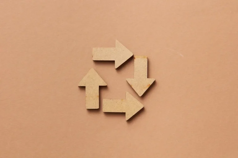 Close-up of a recycling symbol made from wooden arrows on a beige background.