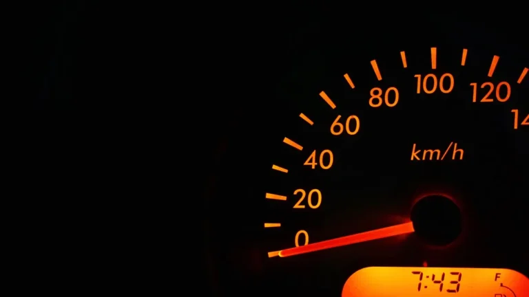 Night view of a car speedometer illuminated in orange, showing kilometers per hour.