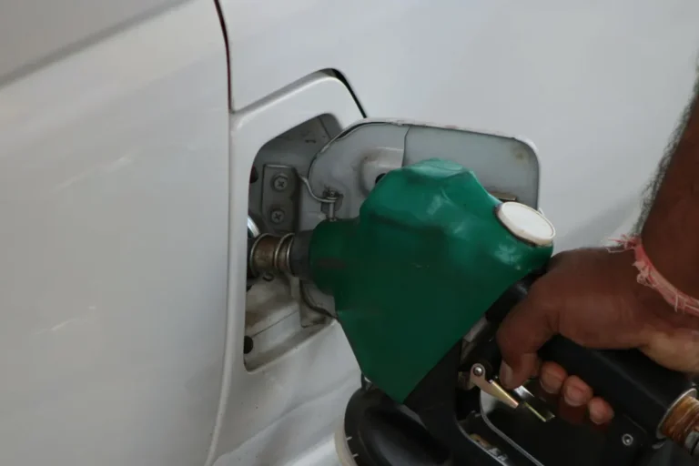 Close-up of a hand refilling a car's gas tank at a station with a green fuel nozzle.