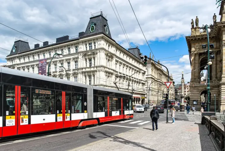 Modern tram passing by historic architecture in Prague, showcasing urban transport and elegant buildings.