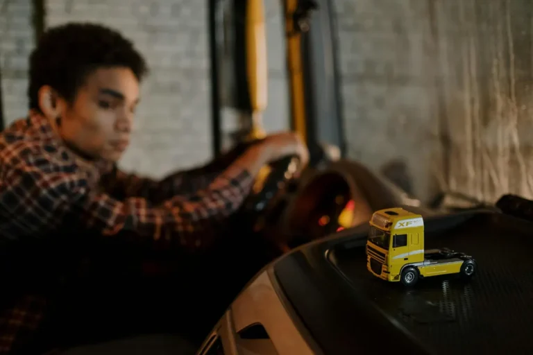 A driver in a truck cab with a focus on a miniature yellow truck toy, creating a blurred background.