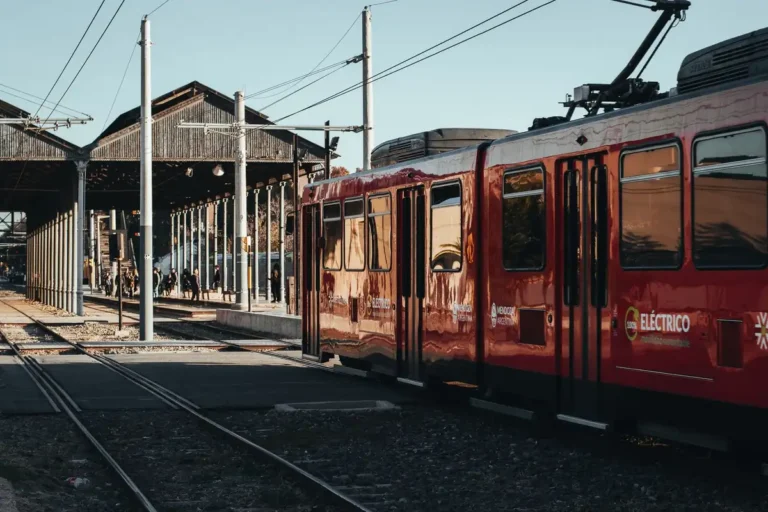 A red electric train at a busy platform in Mendoza, Argentina, during the day.
