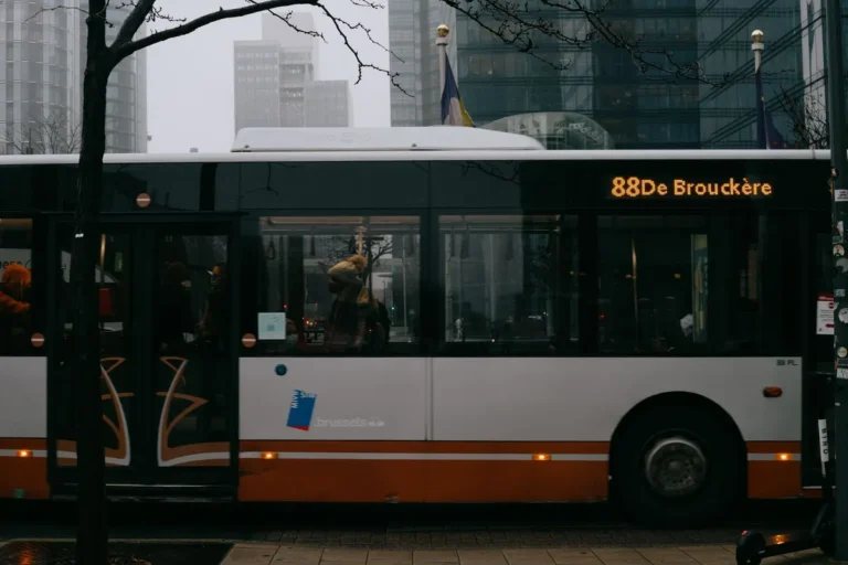 Modern bus with number and inscription on roadway against multistory building facades in city