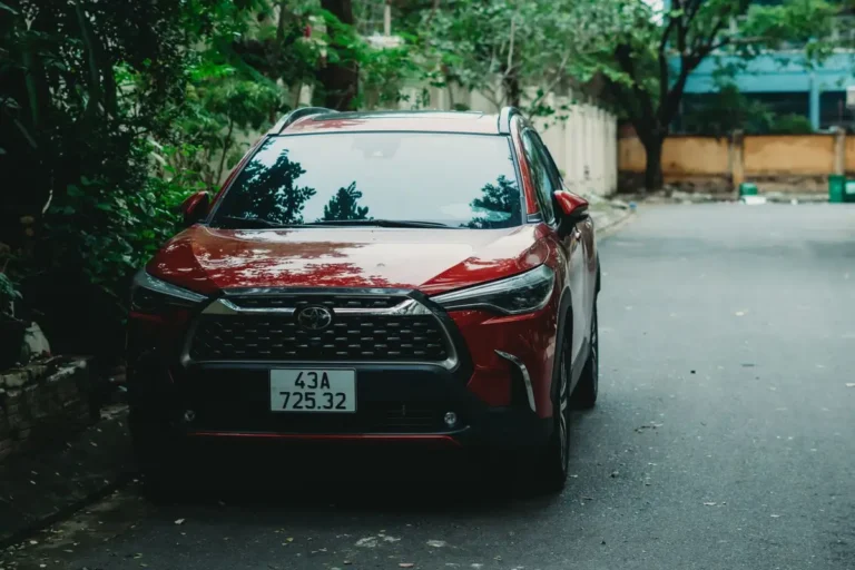 A red Toyota Corolla Cross parked outdoors on a quiet street with greenery.